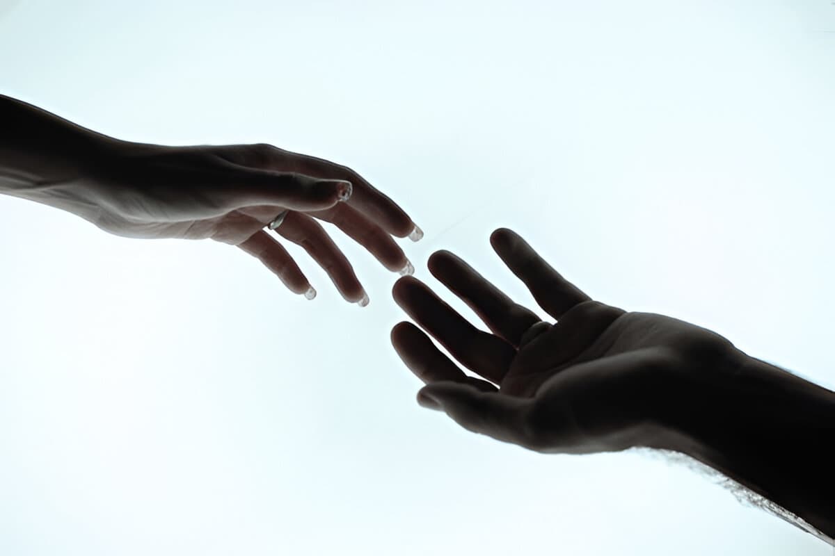 Two hands reaching for each other. One hand is coming into view from the right side shifted slightly to the bottom. The other coming into view from the left side shifted slightly to the top